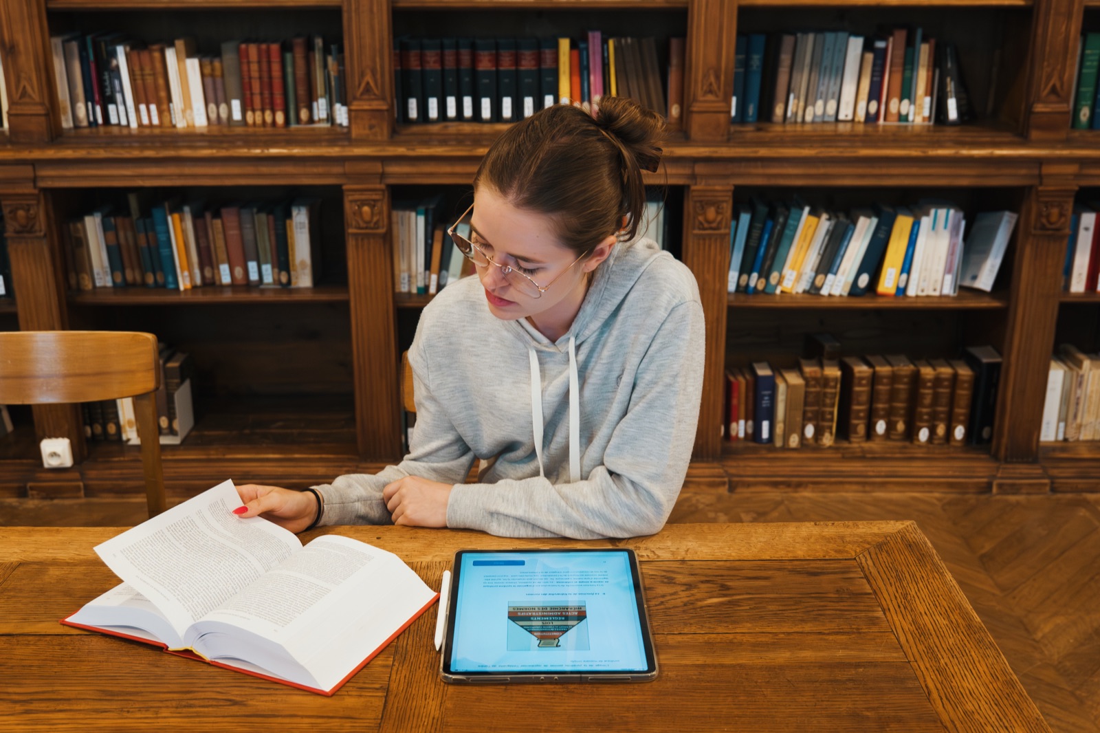 Une élève travaille en bibliothèque universitaire, un ouvrage de droit ouvert à côté de sa tablette.
